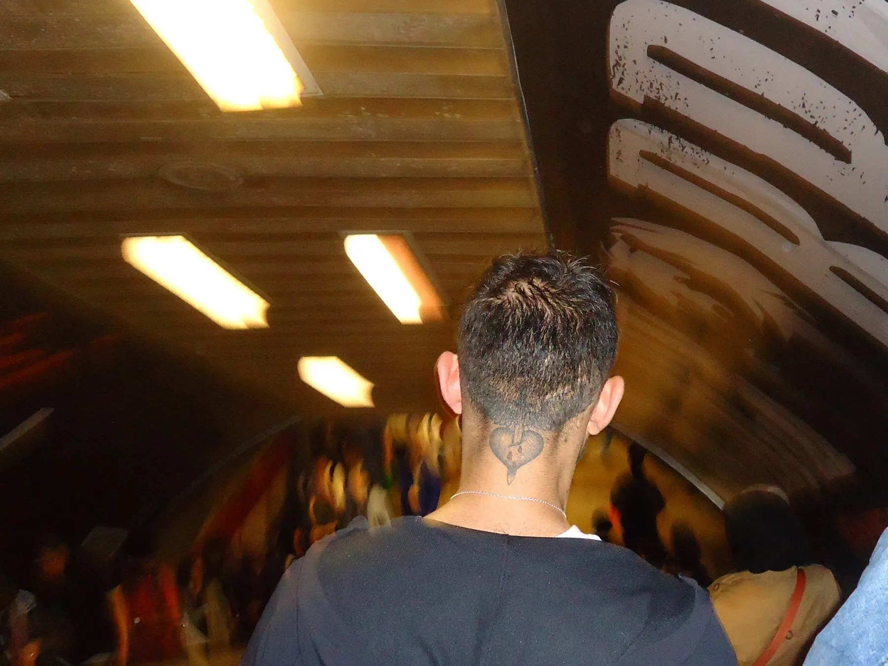 Man with a tattoo on his shaved neck in a crowded tunnel under fluorescent lights