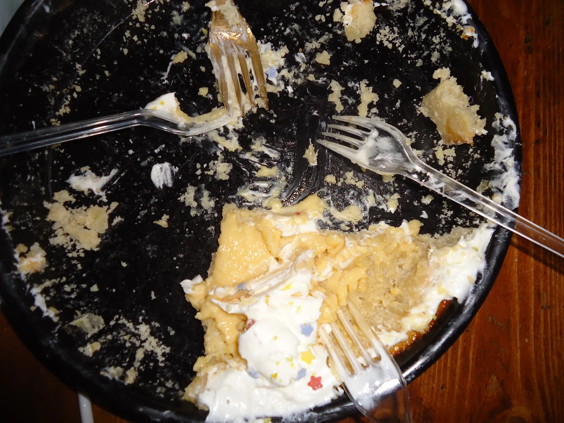 Remains of a cake on a black plate with plastic forks
