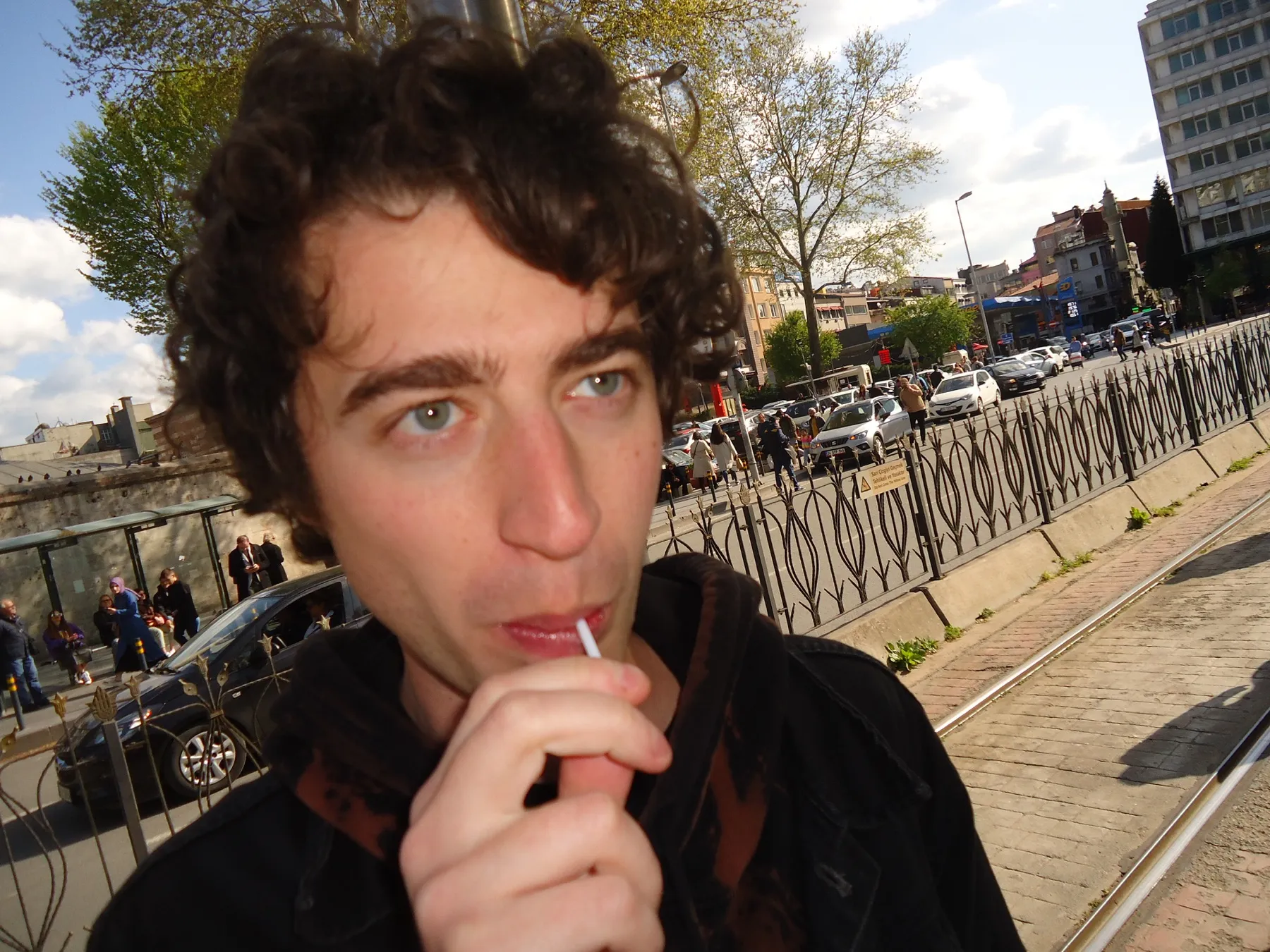 Man with curly hair holding a lollipop by a tram line
