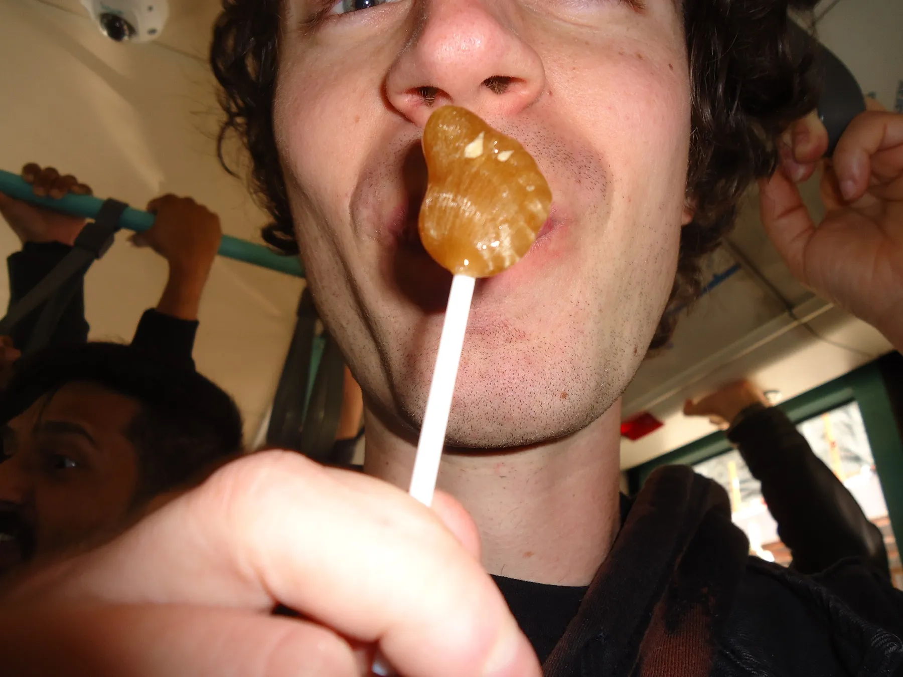 Close-up of a man licking a lollipop on a crowded bus