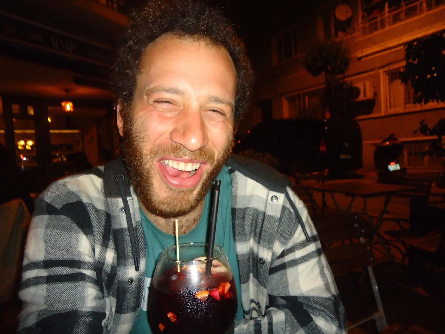 Bearded man laughing with a drink at a table at night