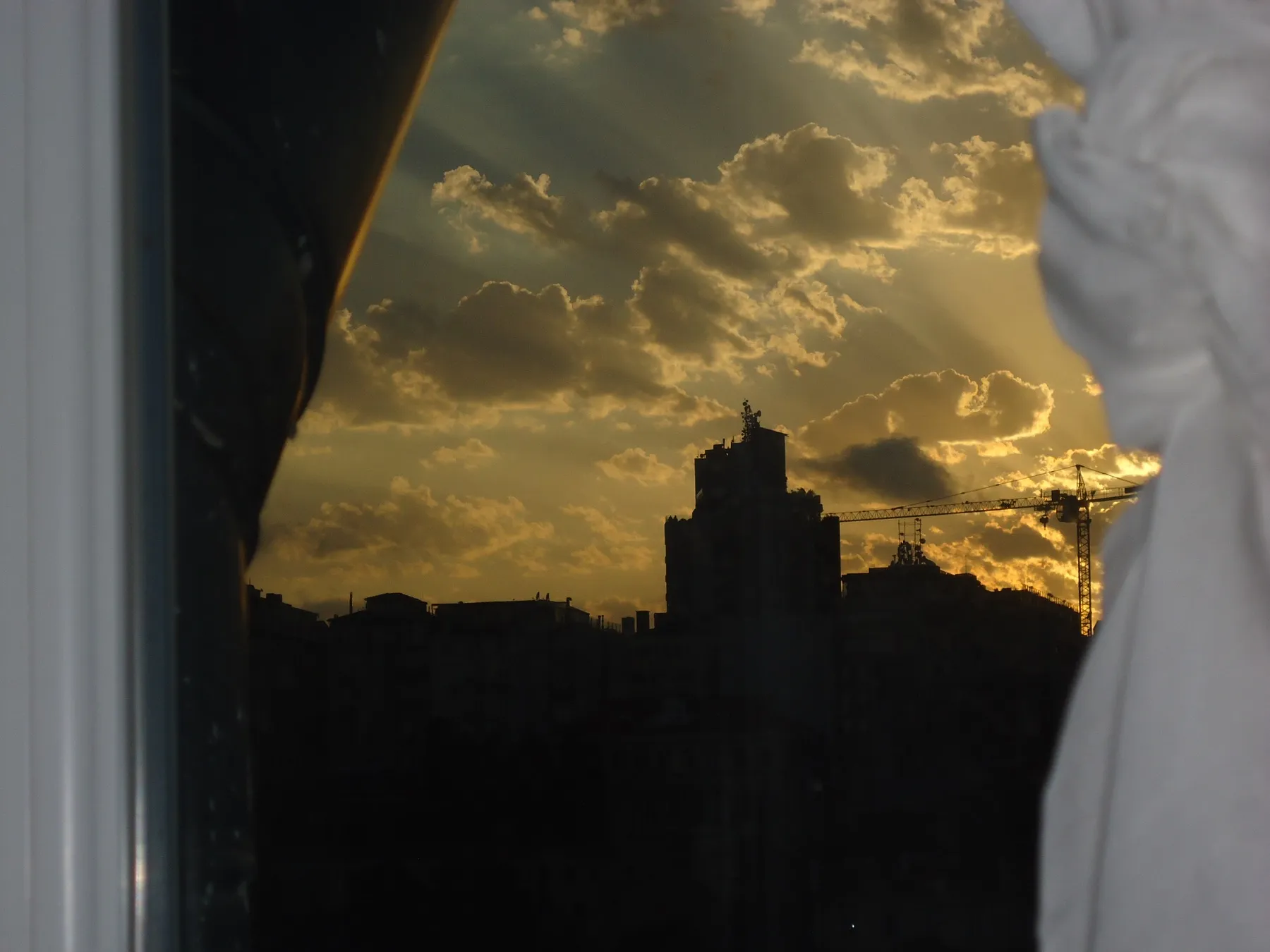 Silhouettes of buildings against a cloudy sunset, seen through a window