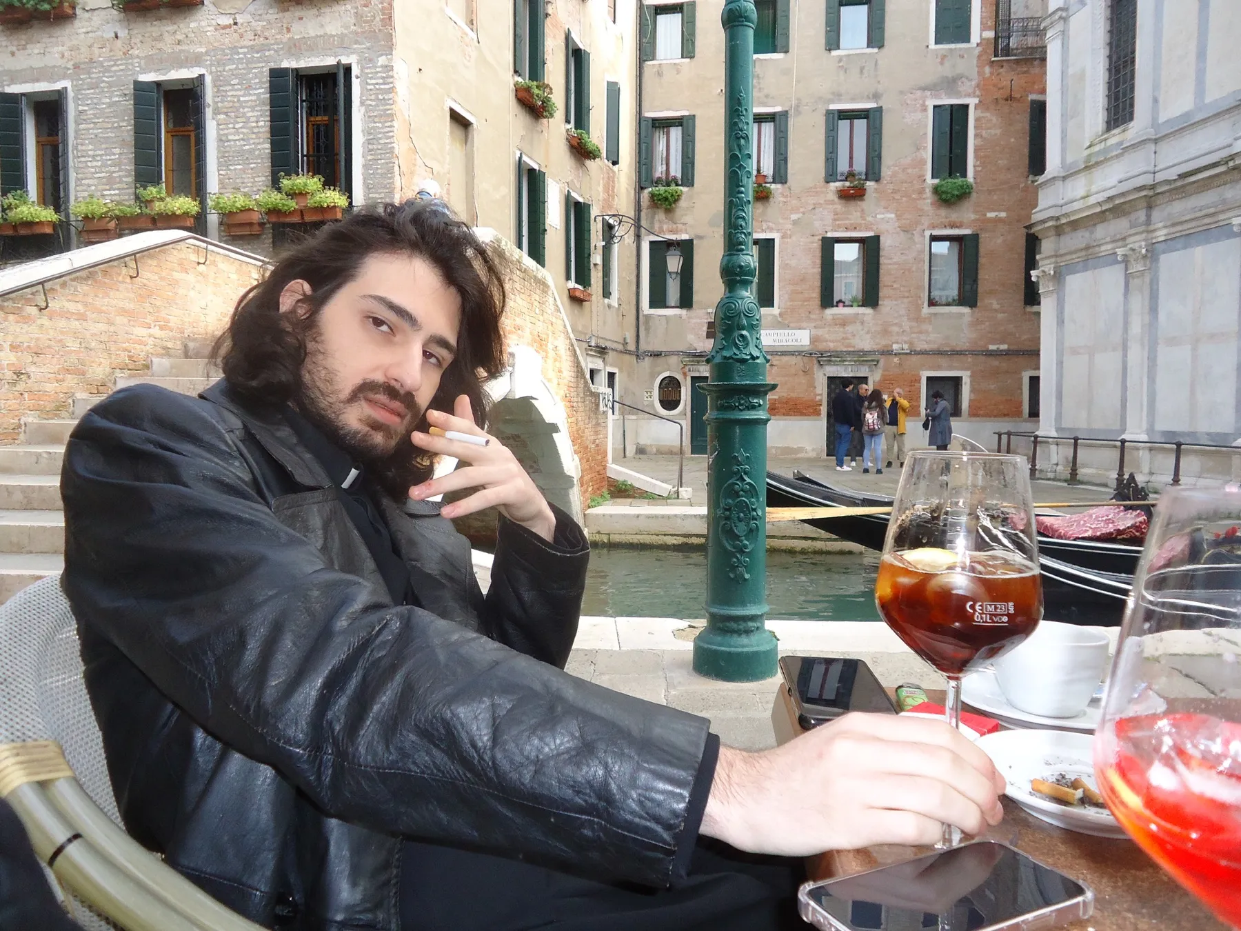 Man in a leather jacket with a drink by a canal in Venice