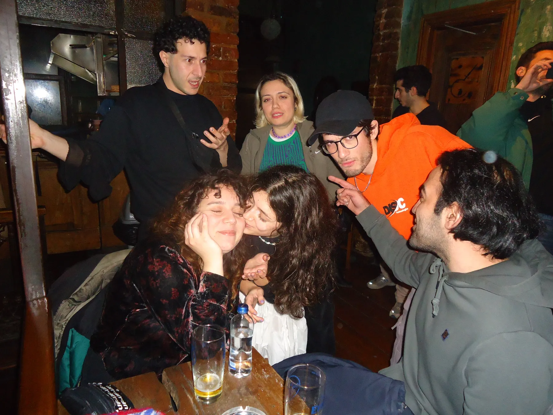 Friends kissing and laughing in a crowded bar