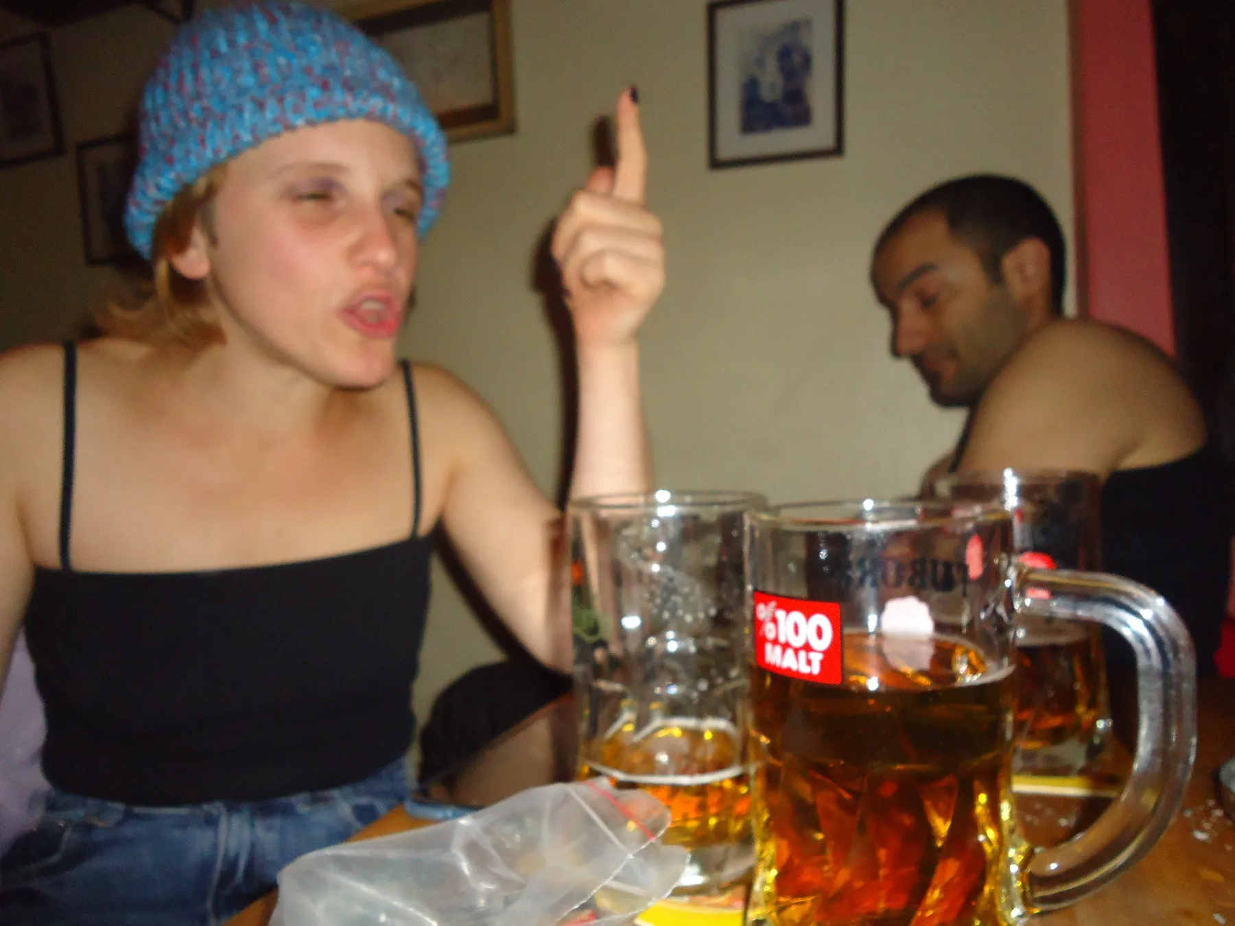 Woman in a blue knitted hat talking at a table with beer mugs