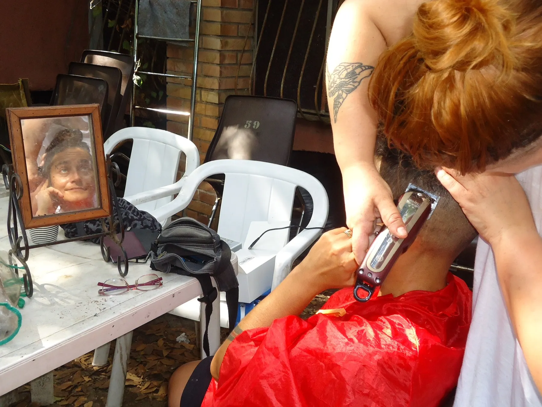 Hairdresser shaving a head, with a framed photo of an older woman on the table
