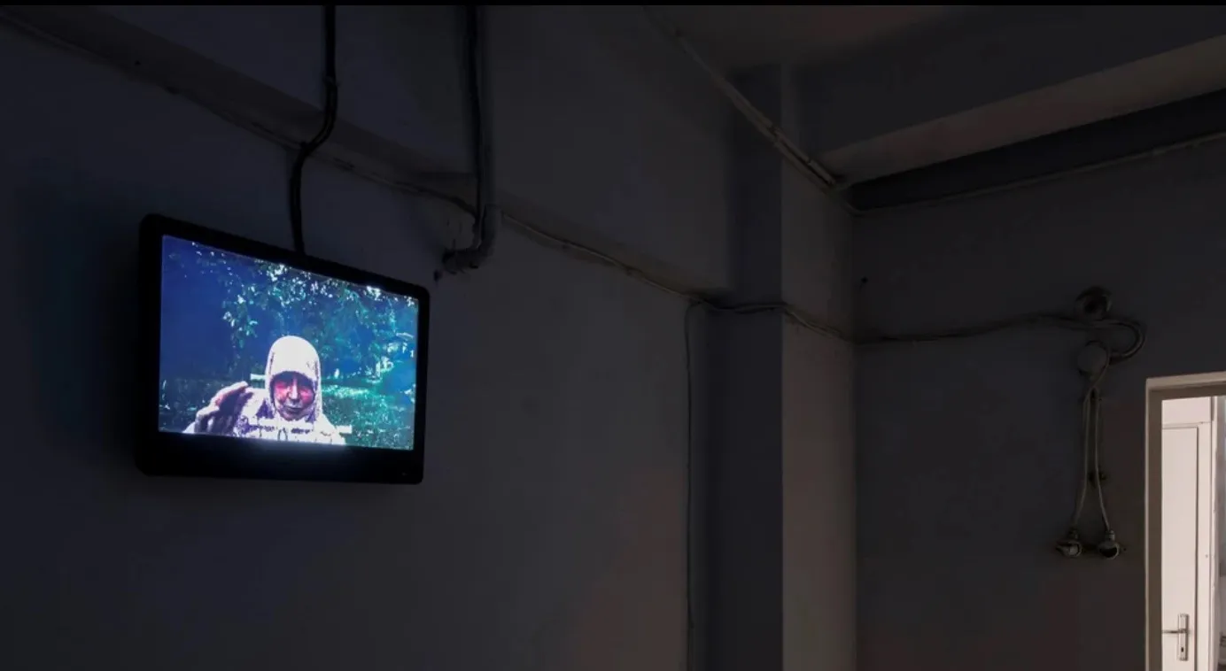 Installation view of Rahm'e: a video playing on a wall-mounted screen in a dark room