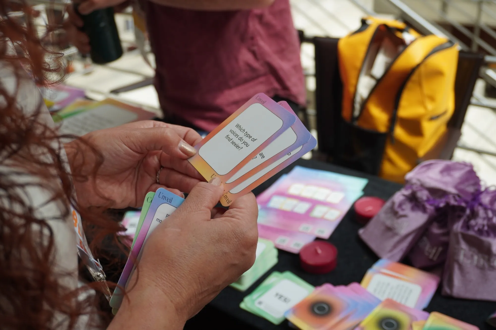 Hands holding Unveil question cards above a table with velvet bags and candles