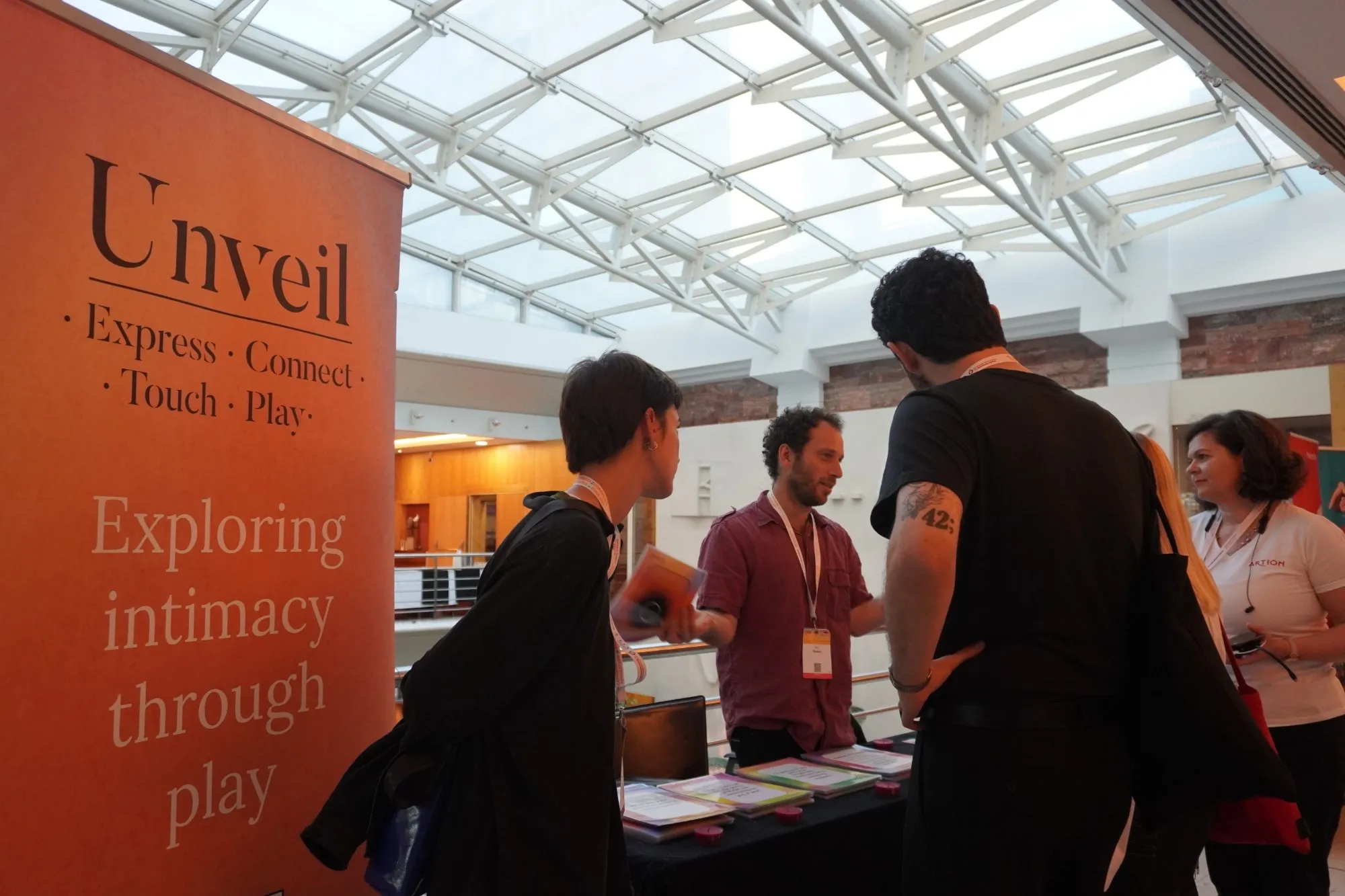 The Unveil stand with a banner reading “Exploring intimacy through play”, visitors talking at the table