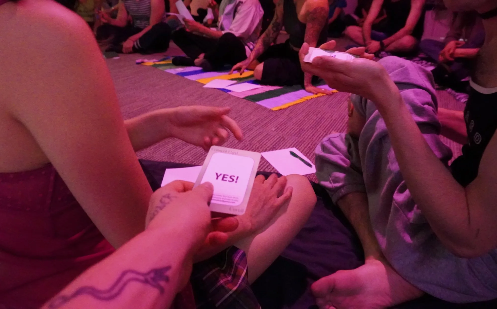 Workshop participants in pink light holding up a YES consent card